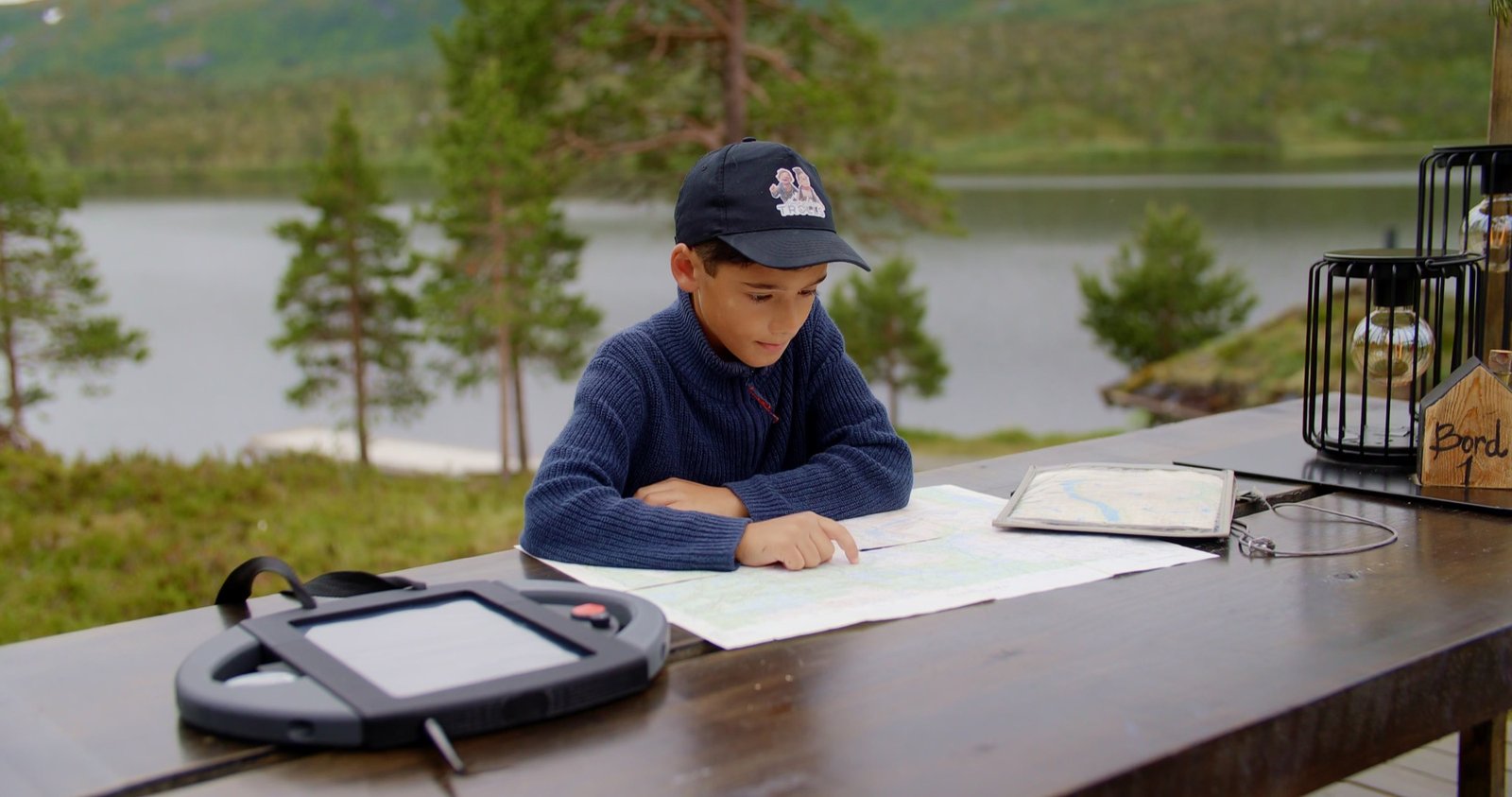 Gutt studerer kartet ved et bord ved Langvatnet, med trolldetektoren foran seg